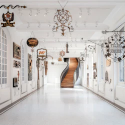 Ett vitt galleri med antika skyltar och skulpturer på väggar och tak, som leder till en böjd trätrappa.