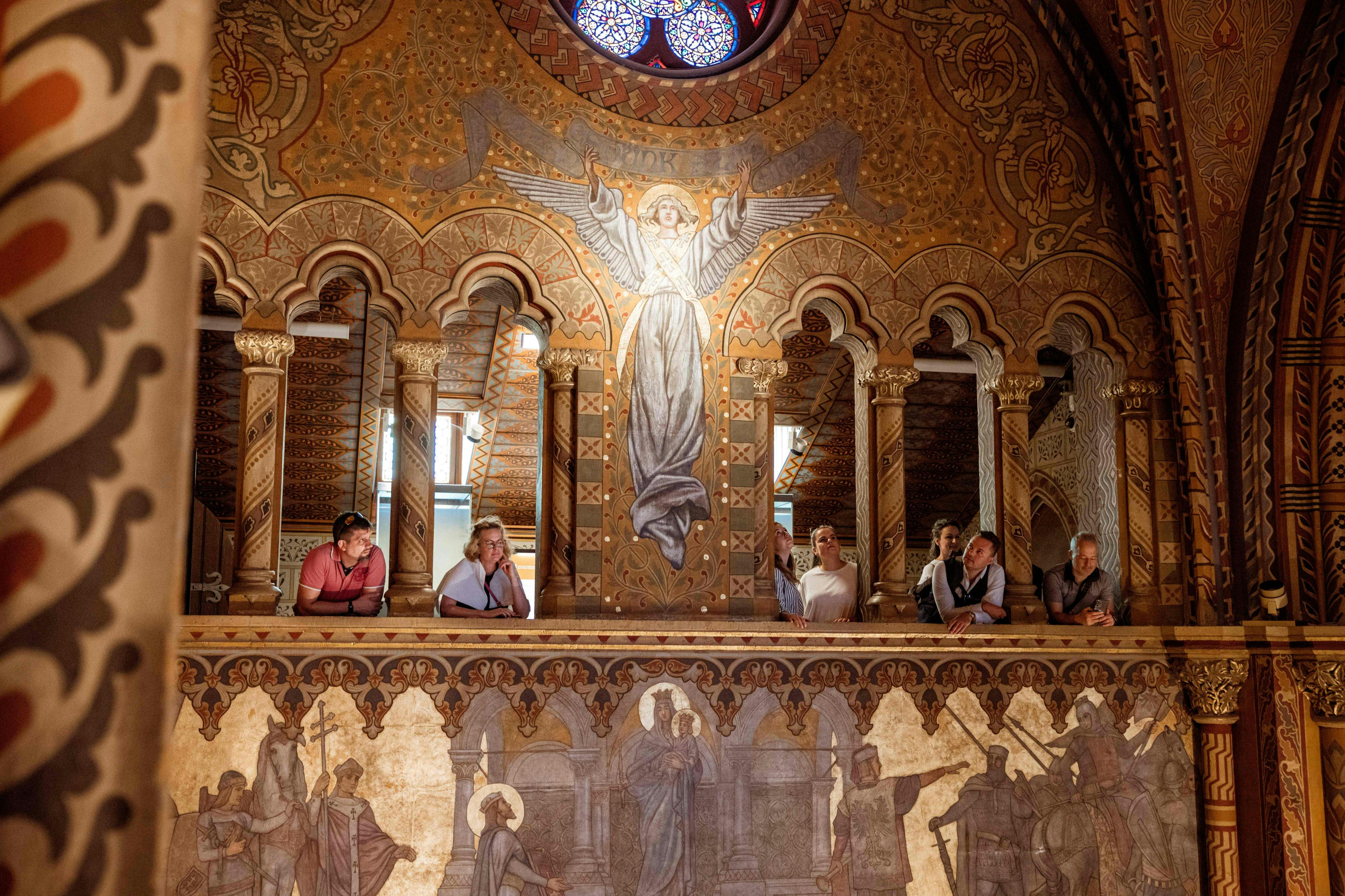 People observing from a balcony in an ornately decorated interior with religious murals and intricate patterns.