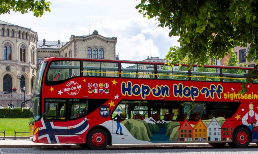 Ein leuchtend roter Doppeldecker-Sightseeing-Bus mit dem Text "Hop On Hop Off" und verschiedenen aufgedruckten Nationalflaggen auf der Seite.