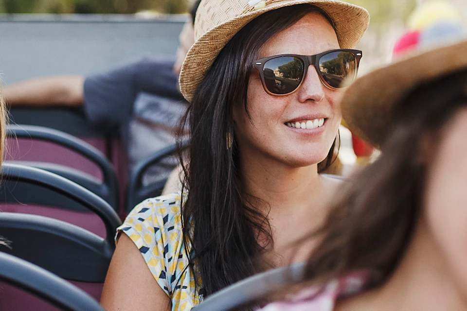 Four women wearing sunglasses and hats smiling while seated on a bus or open-air vehicle.
