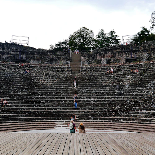 Människor utspridda runt stensätena i en gammal amfiteater med en träscen i förgrunden. Träd syns högst upp.