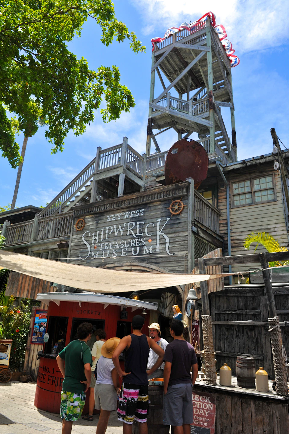 Tourists stand outside the entrance of the Key West Shipwreck Treasures Museum, a wooden building with a tall tower and nautical decor.