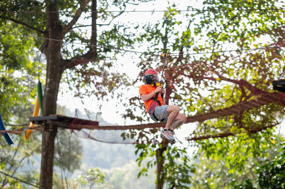 Person ziplining through a forested area, wearing safety gear including a helmet and harness.