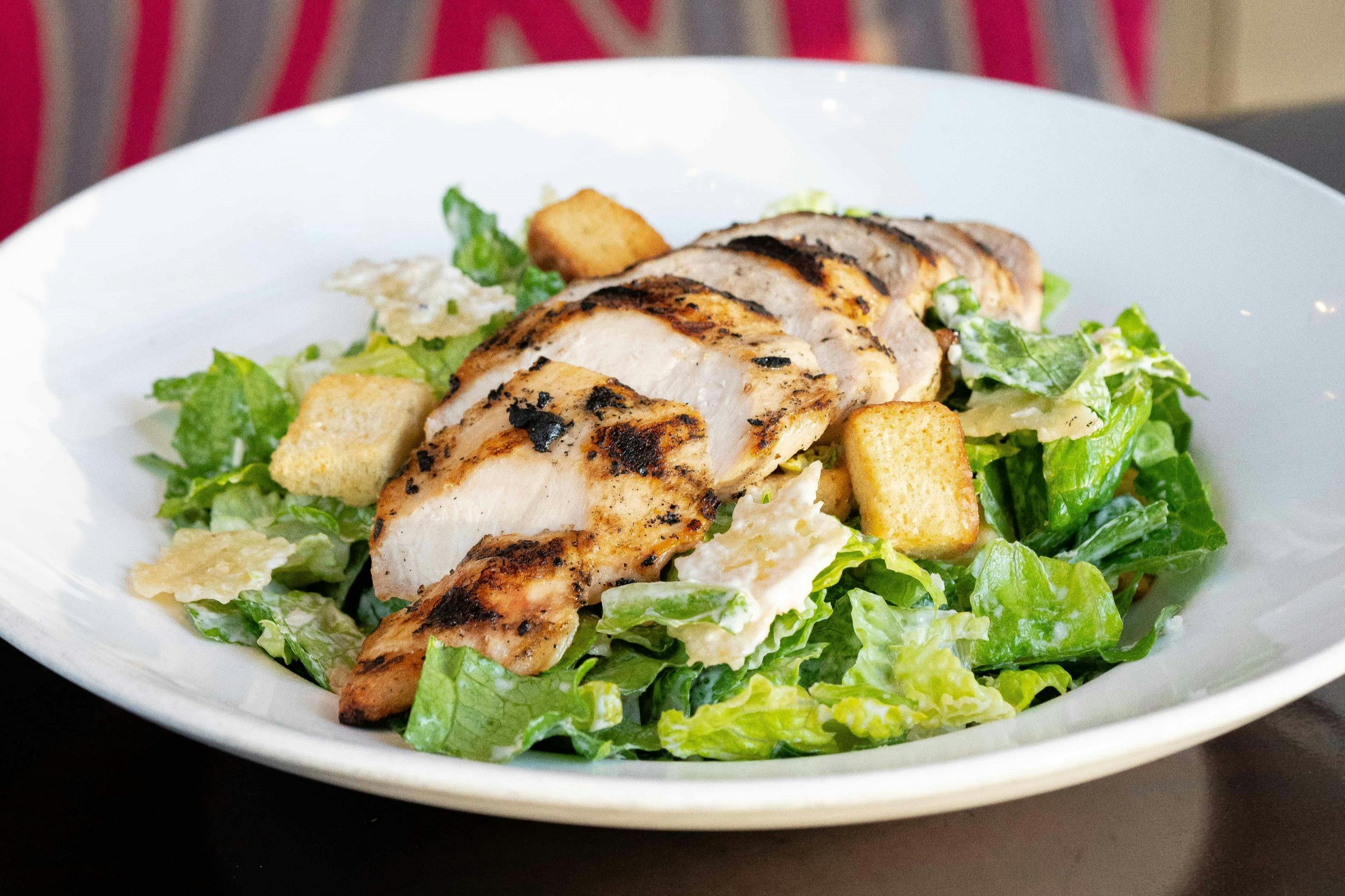 A Caesar salad topped with grilled chicken slices and croutons, served on a white plate.