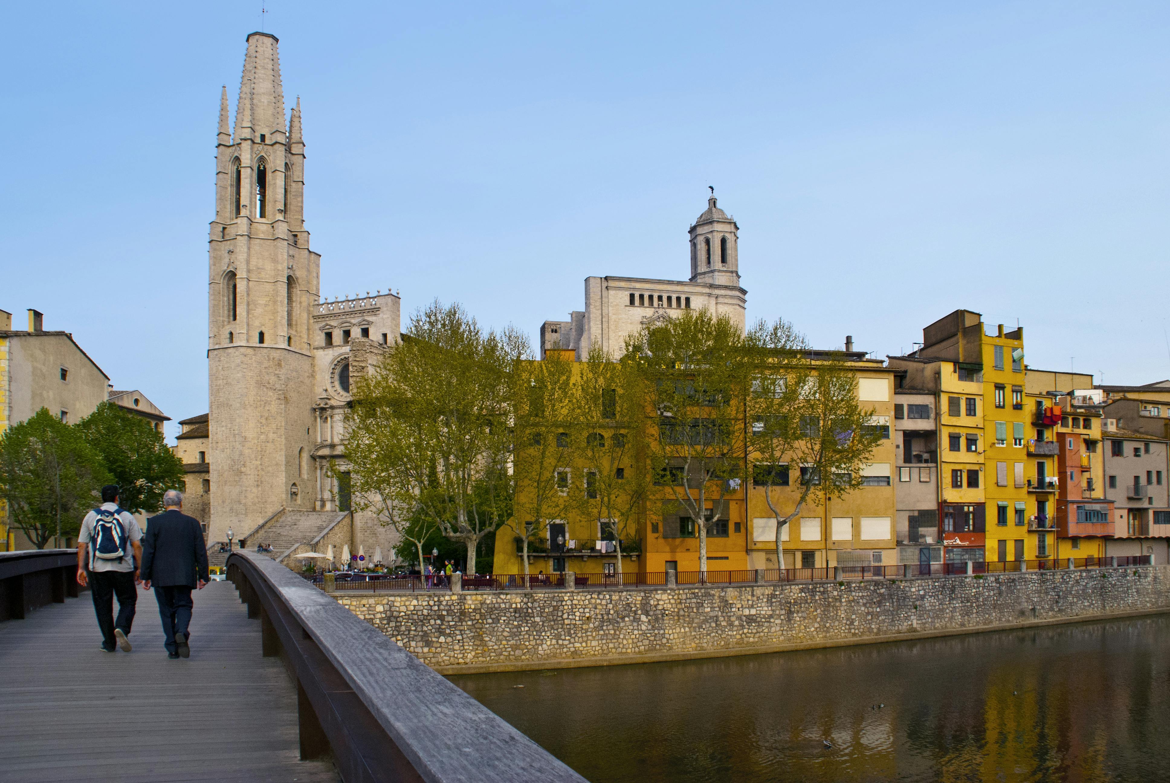 Depuis un pont enjambant une rivière, on aperçoit une église en pierre dotée d'un haut clocher et des bâtiments colorés situés à proximité.