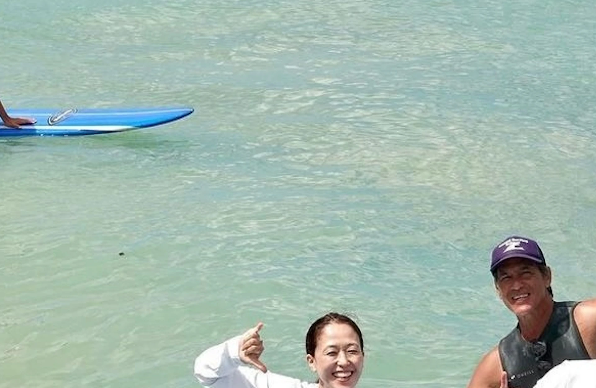 A group of people sitting on surfboards in shallow water, smiling and gesturing positively, with one person standing behind.