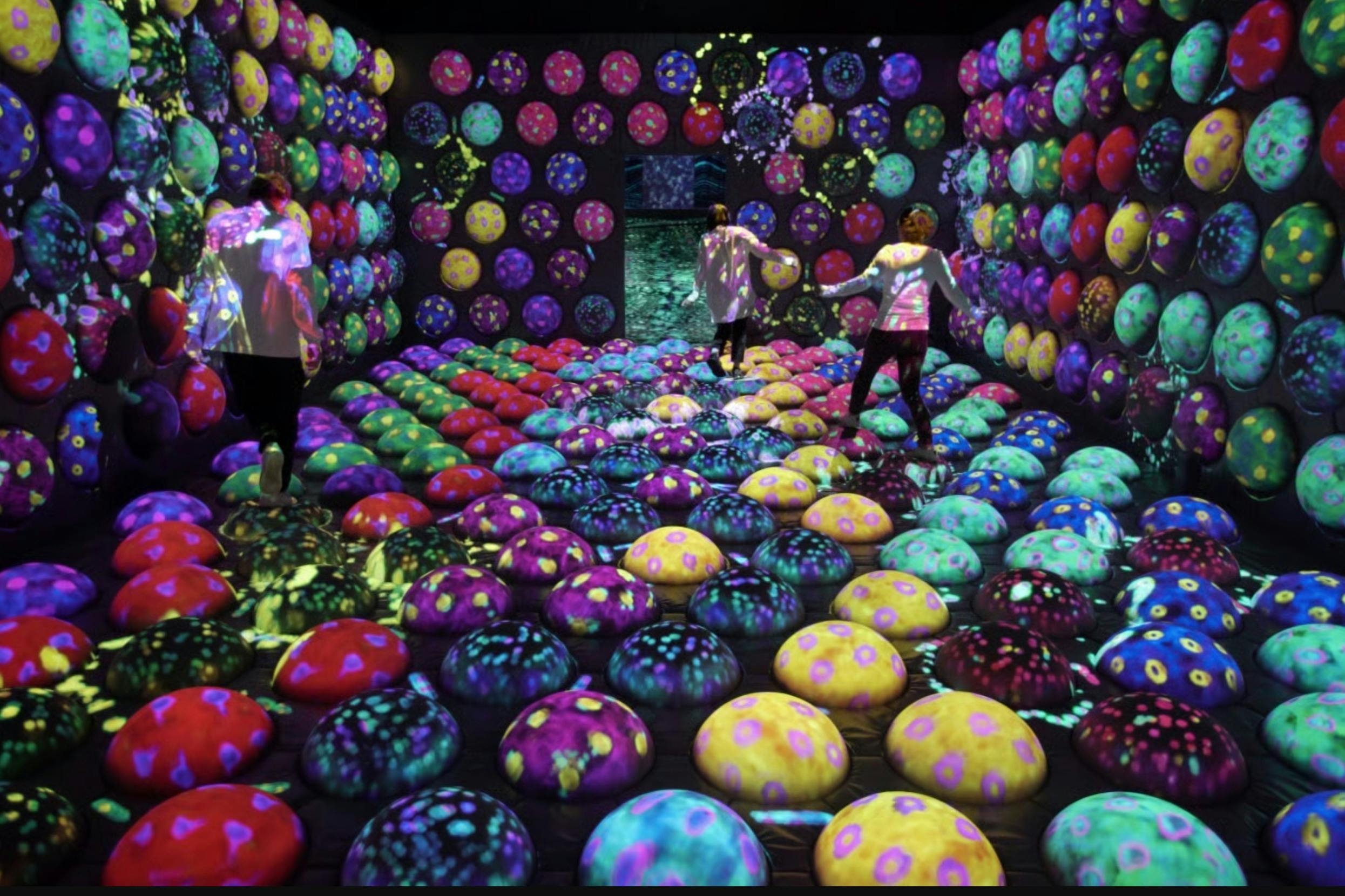 Une pièce colorée avec des coussins aux motifs vifs recouvrant le sol et les murs, où les gens interagissent et explorent.
