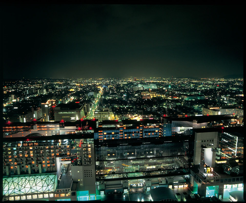 Aerial view of a cityscape at night, with buildings, illuminated streets, and scattered lights stretching towards the horizon.