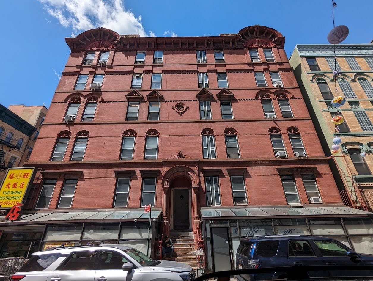 A five-story brick building with arched windows, a central entrance, and a storefront at street level, under a blue sky.