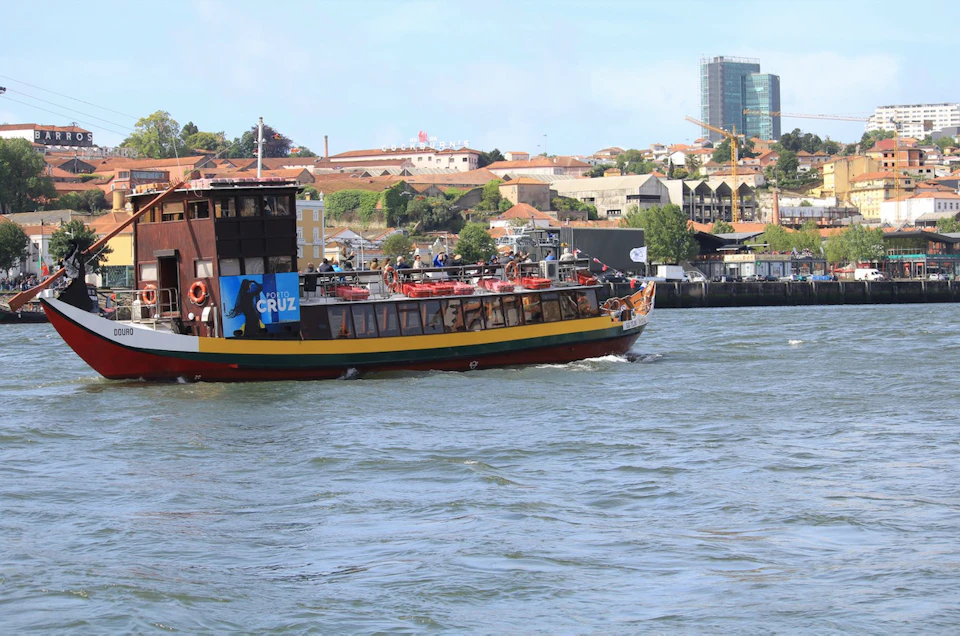 Tour boat cruising on a river with a cityscape, featuring buildings and greenery, visible in the background.