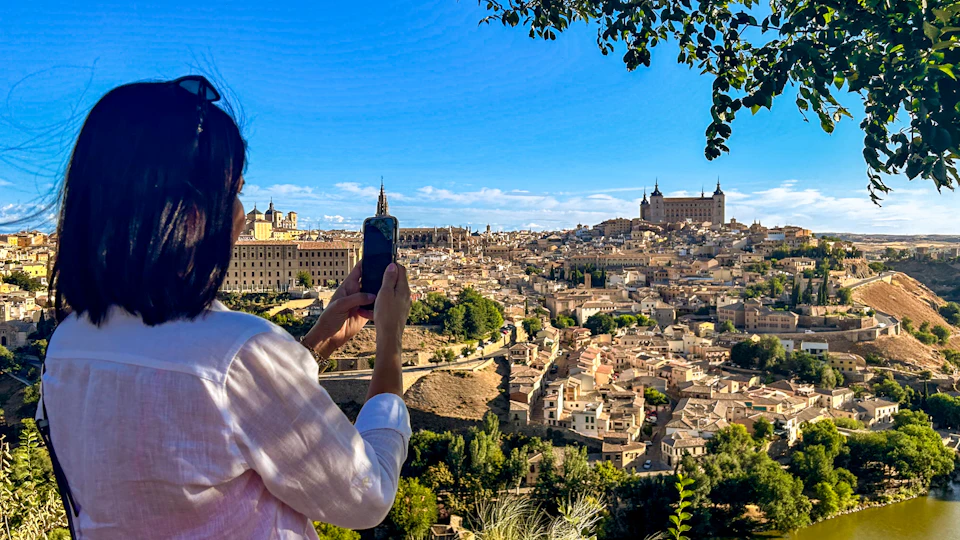 Person in a white shirt taking a photo of a historic cityscape with many buildings, under a clear blue sky.
