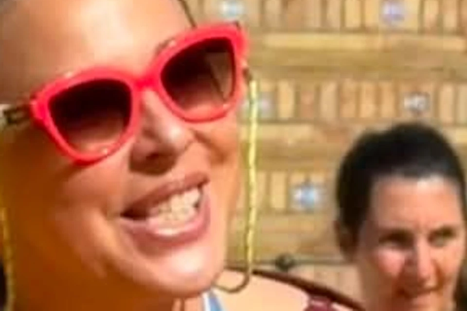 A woman wearing sunglasses and a maroon blouse smiles as she chats with others outdoors.