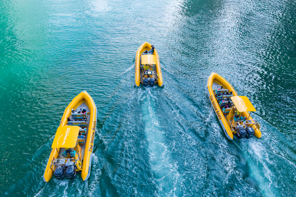 Three yellow speedboats on blue-green water, viewed from above, carrying passengers.