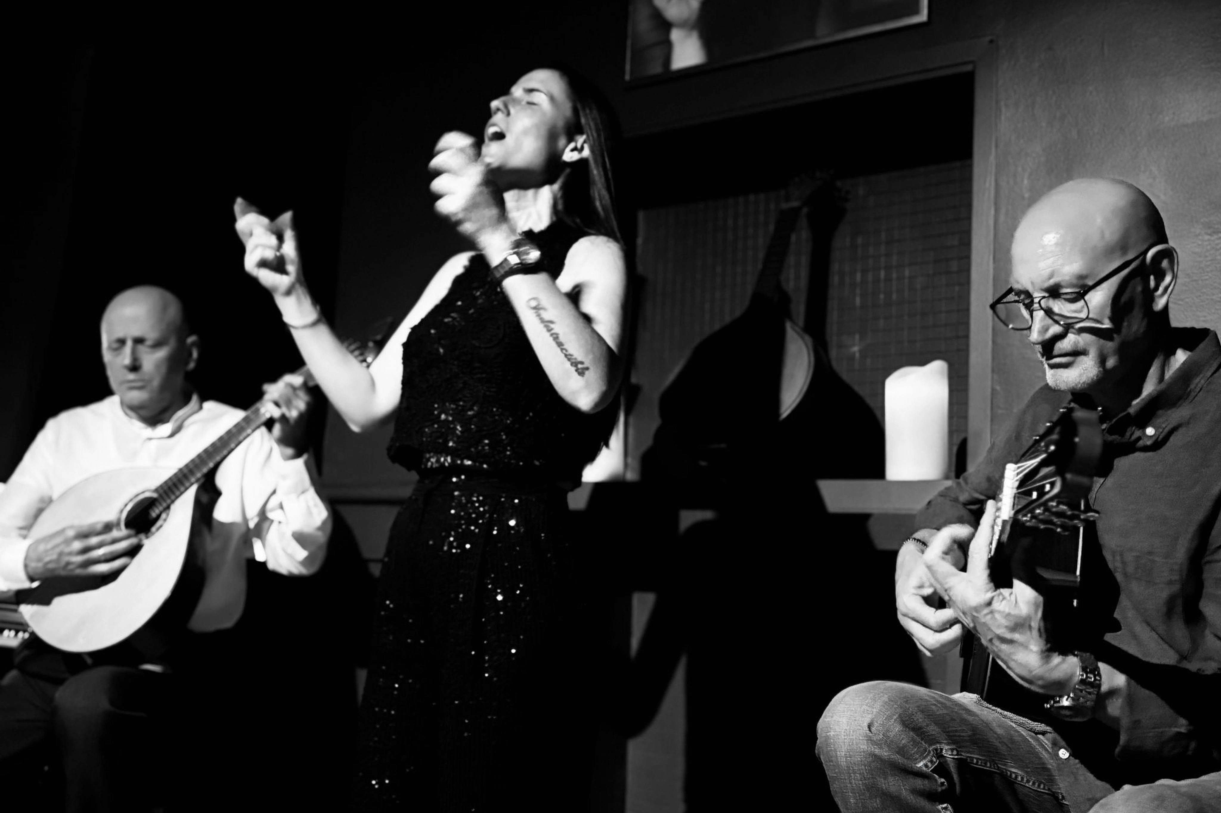 A black and white image of a woman singing passionately and a man playing a string instrument in a dimly lit setting.
