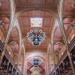 En utsmyckad interiör med höga bågar, detaljerade tak, flera ljuskronor och övre gångbanor med träräcken.