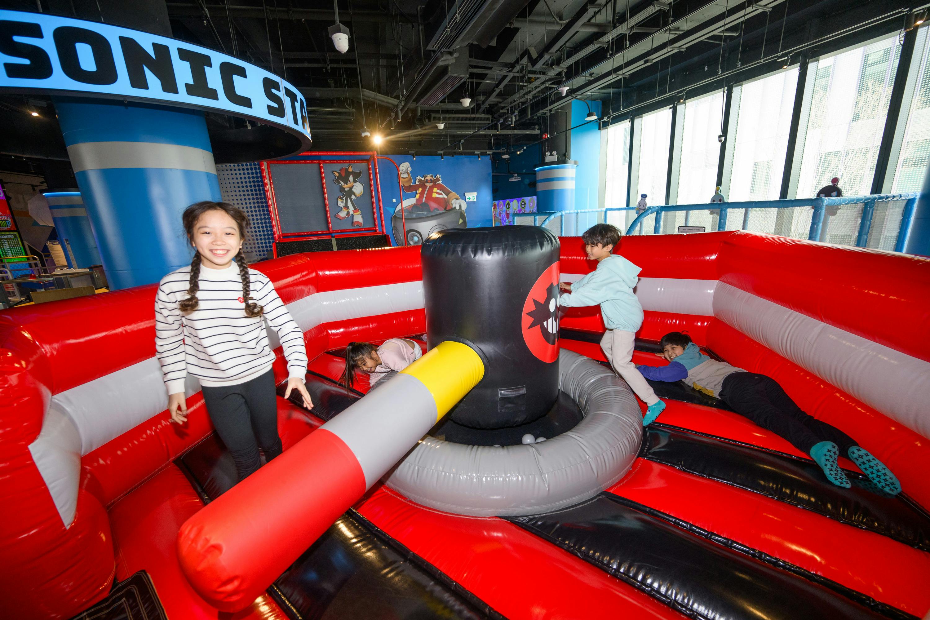 Children playing in an inflatable play area with a rotating obstacle, indoors, under a sign reading "Sonic Station."