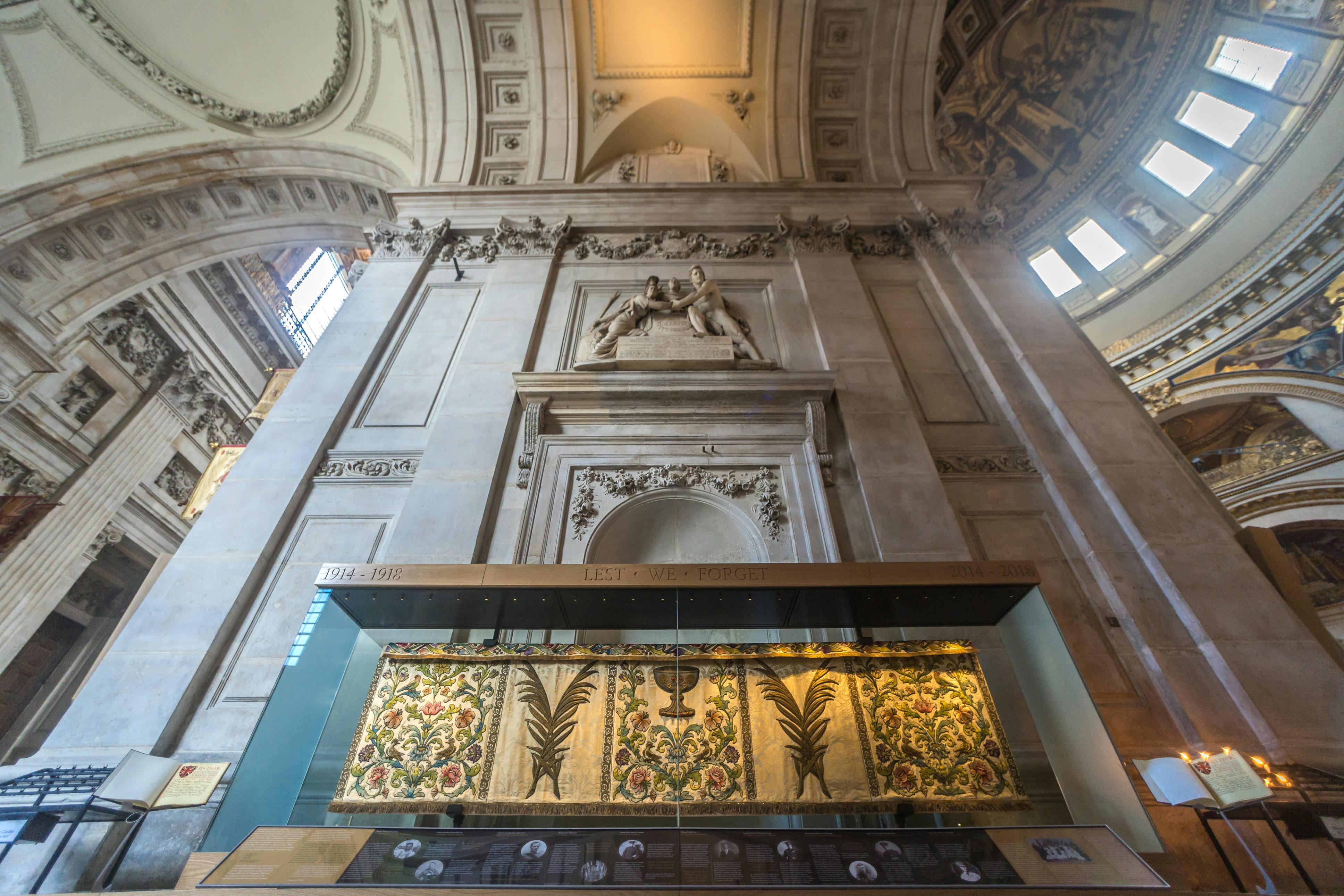 Ornate interior of a grand building with intricate carvings, high arched ceilings, and a glass display case featuring colorful artwork.