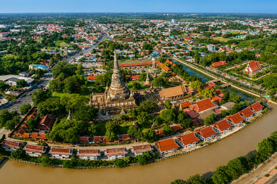Aerial view of a temple complex surrounded by trees, a cityscape, and a river in a sunny area.