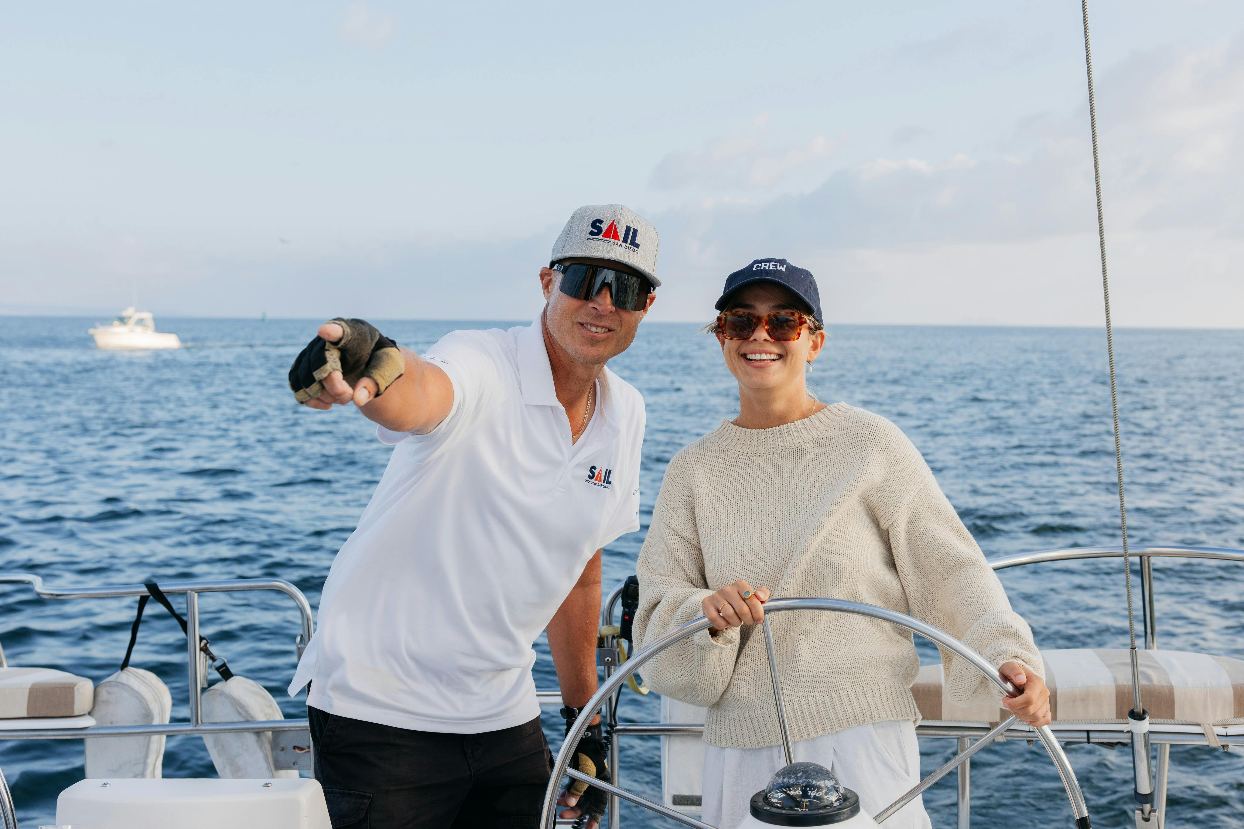 Sail San Diego captain pointing in the distance while a guest stands behind the helm of the boat smiling