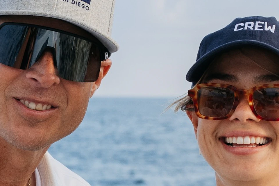 Sail San Diego captain pointing in the distance while a guest stands behind the helm of the boat smiling