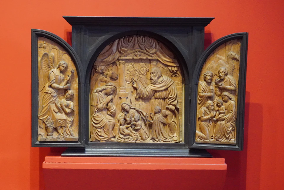A carved wooden triptych depicting religious scenes, displayed against a red wall.