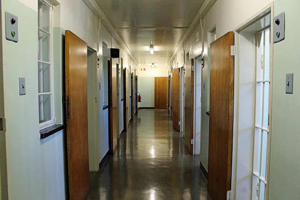A long corridor with several open wooden doors on each side, lit by overhead lights.