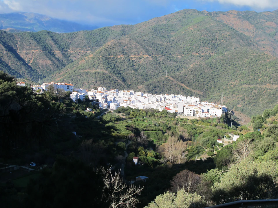 A white village nestled among green hills under a partly cloudy sky.