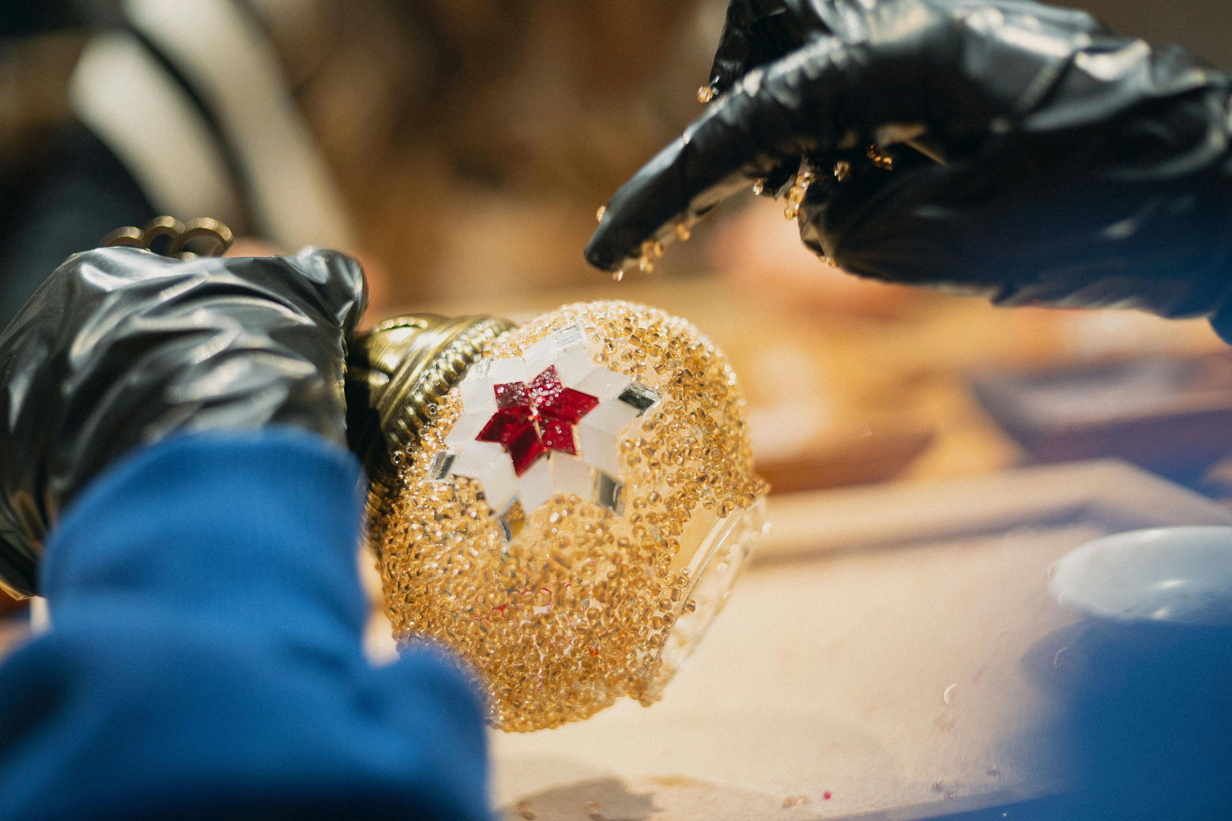 双手戴着黑色手套的特写镜头，用金色和红色宝石装饰马赛克灯。