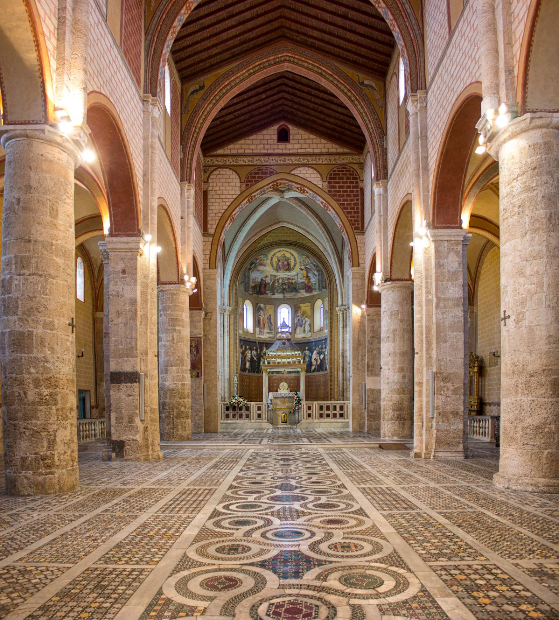 Interior of a grand church with ornate columns, detailed tiled floor, and an illuminated altar in the background.