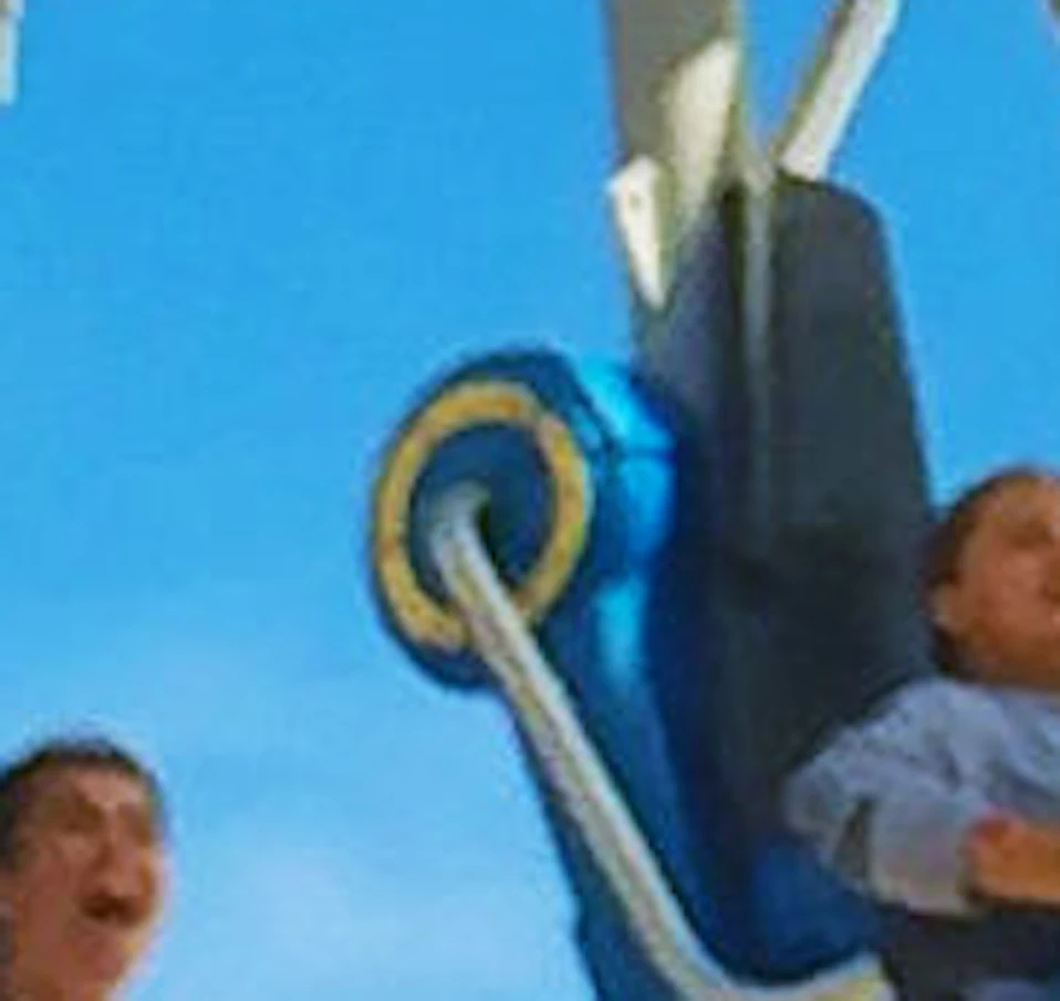 People riding a yellow and blue rollercoaster under a bright blue sky, with legs dangling from the suspended seats.