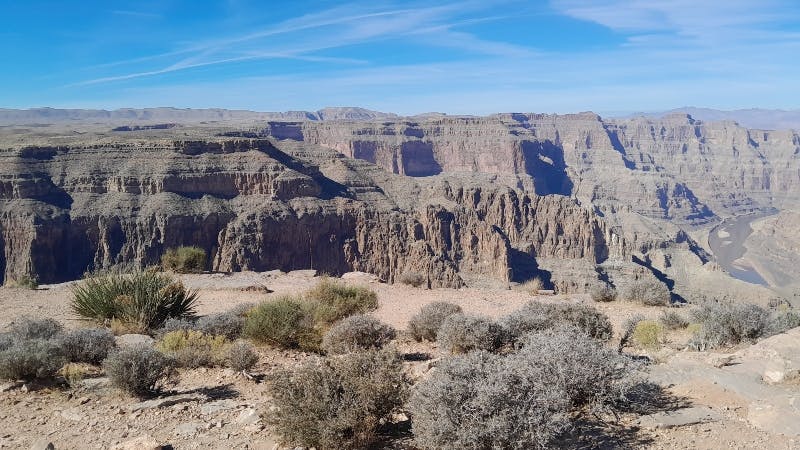 Barren desert landscape with rocky formations and sparse vegetation under a clear blue sky.