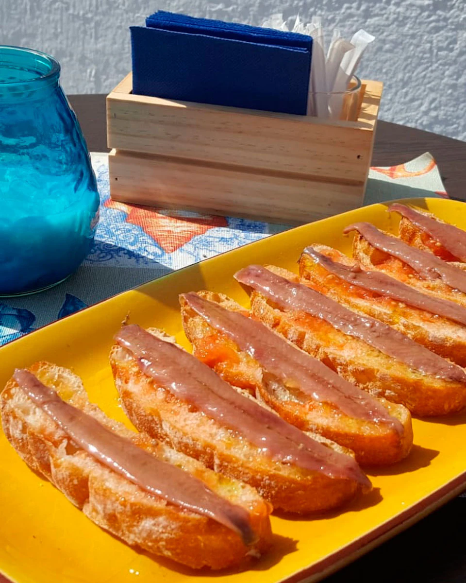 Slices of toasted bread with a reddish-brown spread on a yellow plate, beside a blue glass jar and a wooden napkin holder.