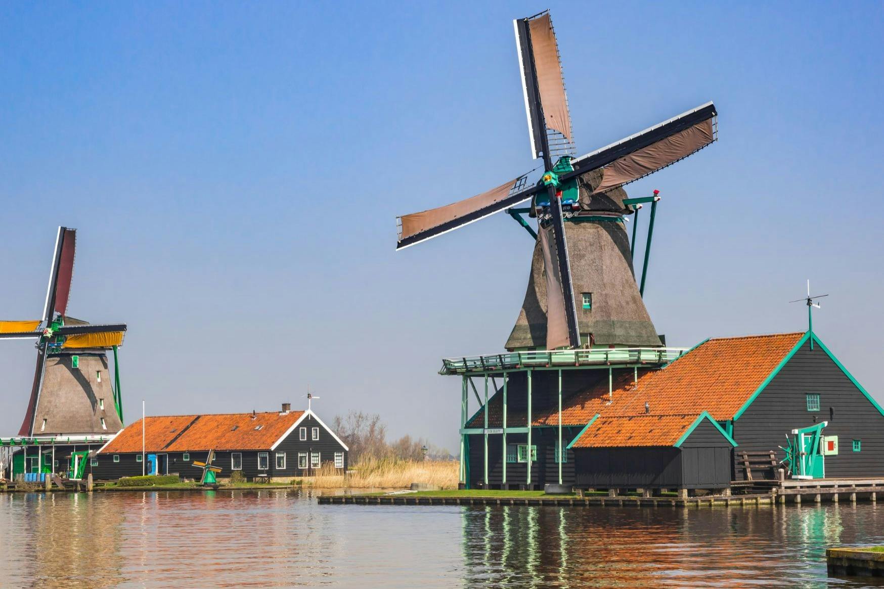 晴れた日には、穏やかな水路のそばにある赤い屋根の建物の隣には、大きな羽根を持つ風車があります。
