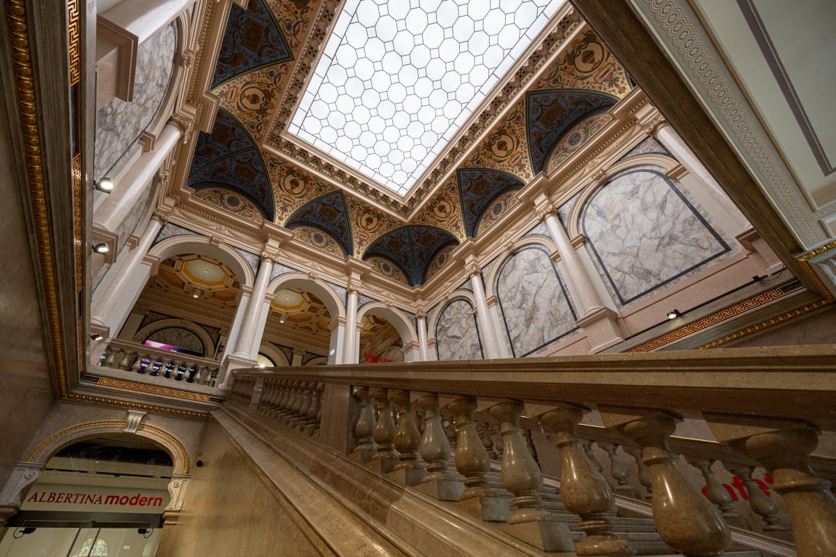 Грандиозный интерьер с декоративными арками, мраморными стенами, декоративным потолком и лестницей с детализированными перилами.