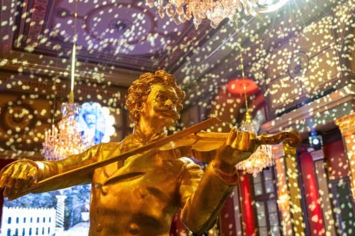 En guldstatue af en violinist i et rigt dekoreret rum med lysekroner og festlig belysning.