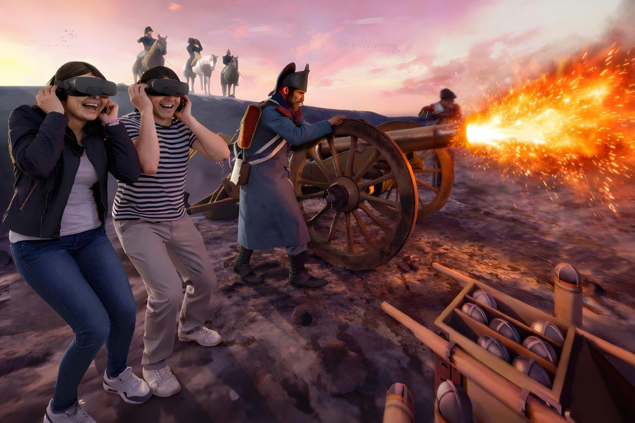 Two people wearing VR headsets appear immersed in a historical battle scene with cannons and soldiers in the background.
