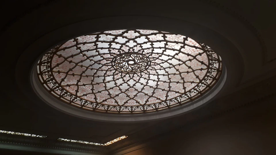 An intricate, oval-shaped stained glass ceiling with symmetrical geometric patterns and delicate floral designs.