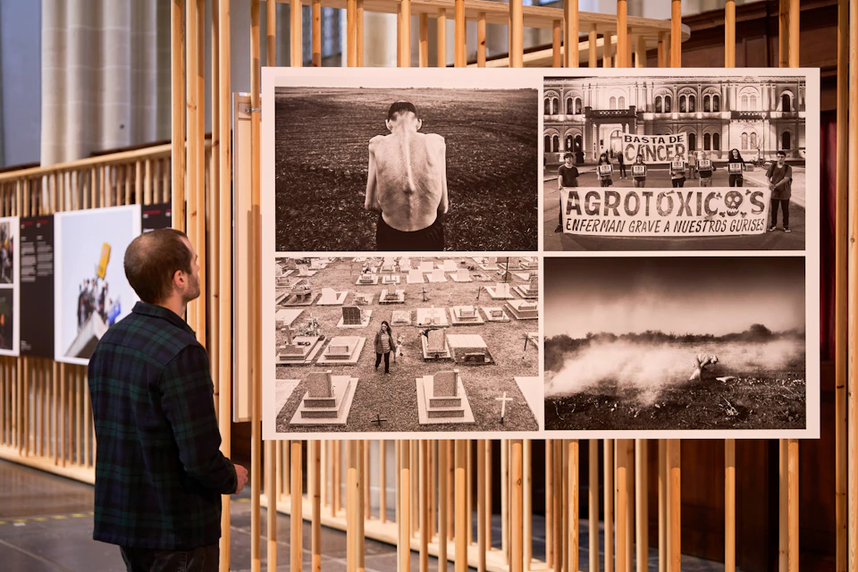 A person observes a display of four black-and-white photos in a gallery, each depicting social and environmental themes.