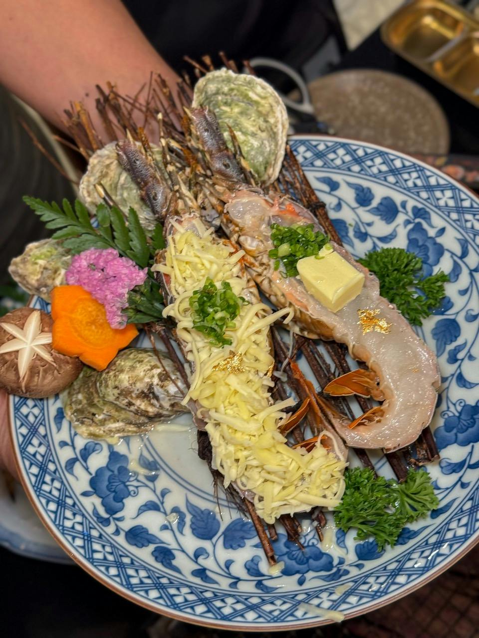 A plate of grilled seafood garnished with herbs, grated cheese, and vegetables, served on a blue patterned dish.