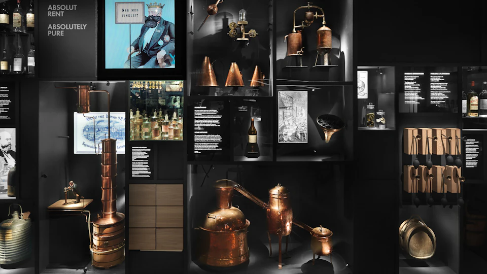 Display of vintage distillation equipment, copper apparatus, historical photographs, and various artifacts in a museum setting.