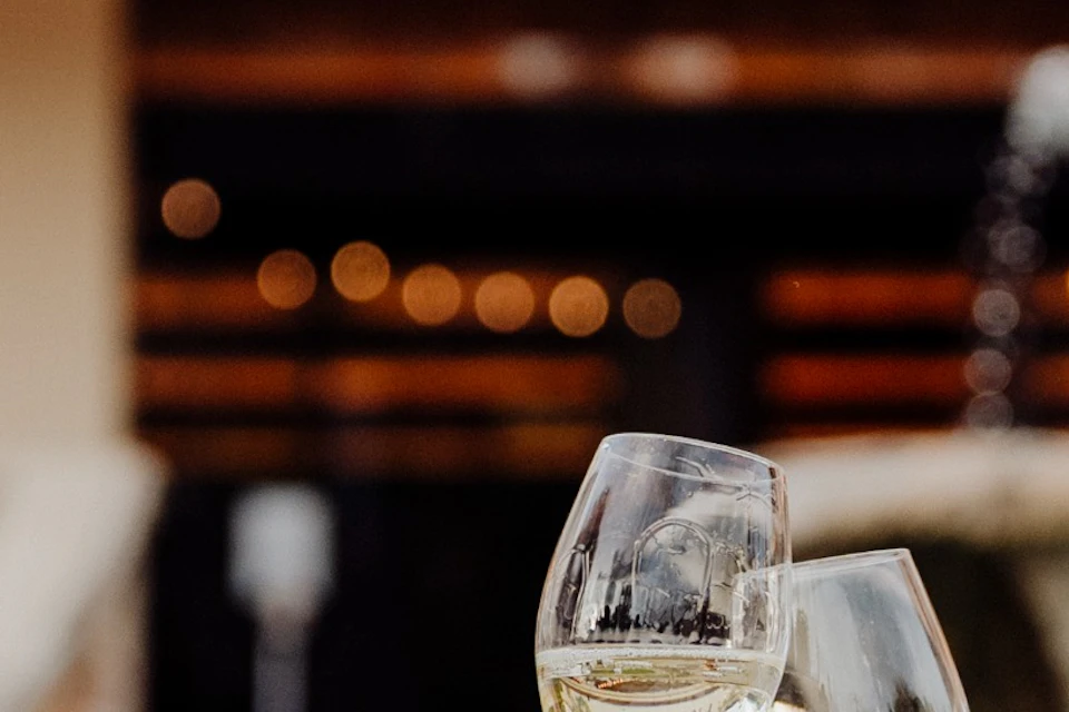 A person in a white shirt clinks wine glasses with another person outside a building adorned with the text "Cavas Freixenet."
