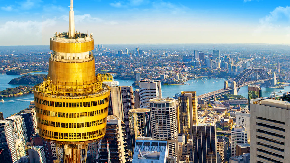 Aerial view of a cityscape with skyscrapers, a prominent golden tower, and a river winding through the city.