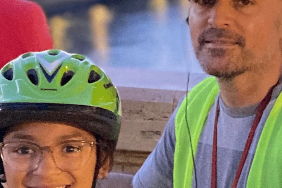 Adult and child wearing safety vests and helmets, posing outdoors at night near a body of water.