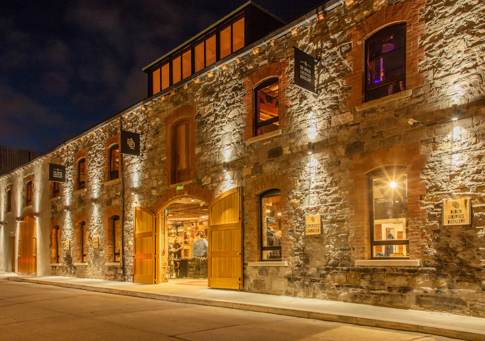 Brick building with arched windows and wooden doors lit up at night. A person is visible inside through the open door.