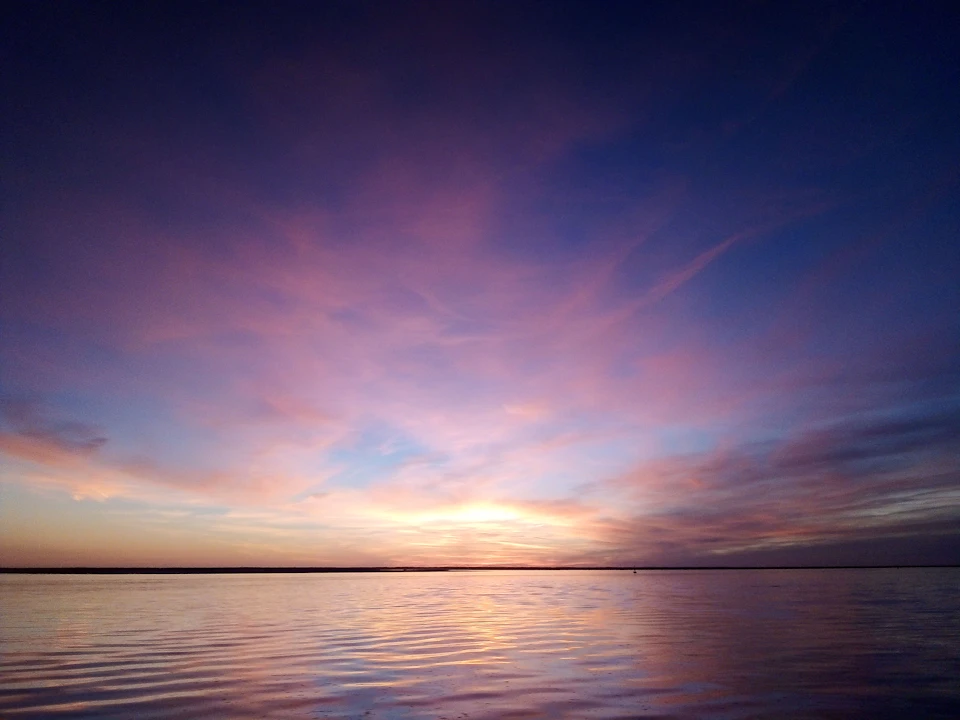 A tranquil sunset over calm water with a sky filled with pink, orange, and purple hues.