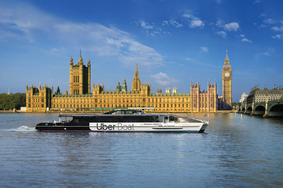 A boat labeled 'Uber Boat by Thames Clippers' on the River Thames, with the Houses of Parliament and Big Ben in the background.