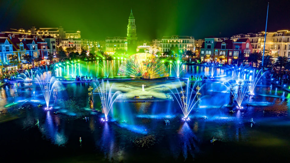 A nighttime water and light show featuring colorful fountains, a central performer, and a vibrant illuminated backdrop.