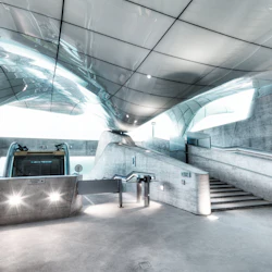 En modern tågstation med ett snyggt, böjt tak, en rulltrappa i mitten och trappor på höger och vänster sida.