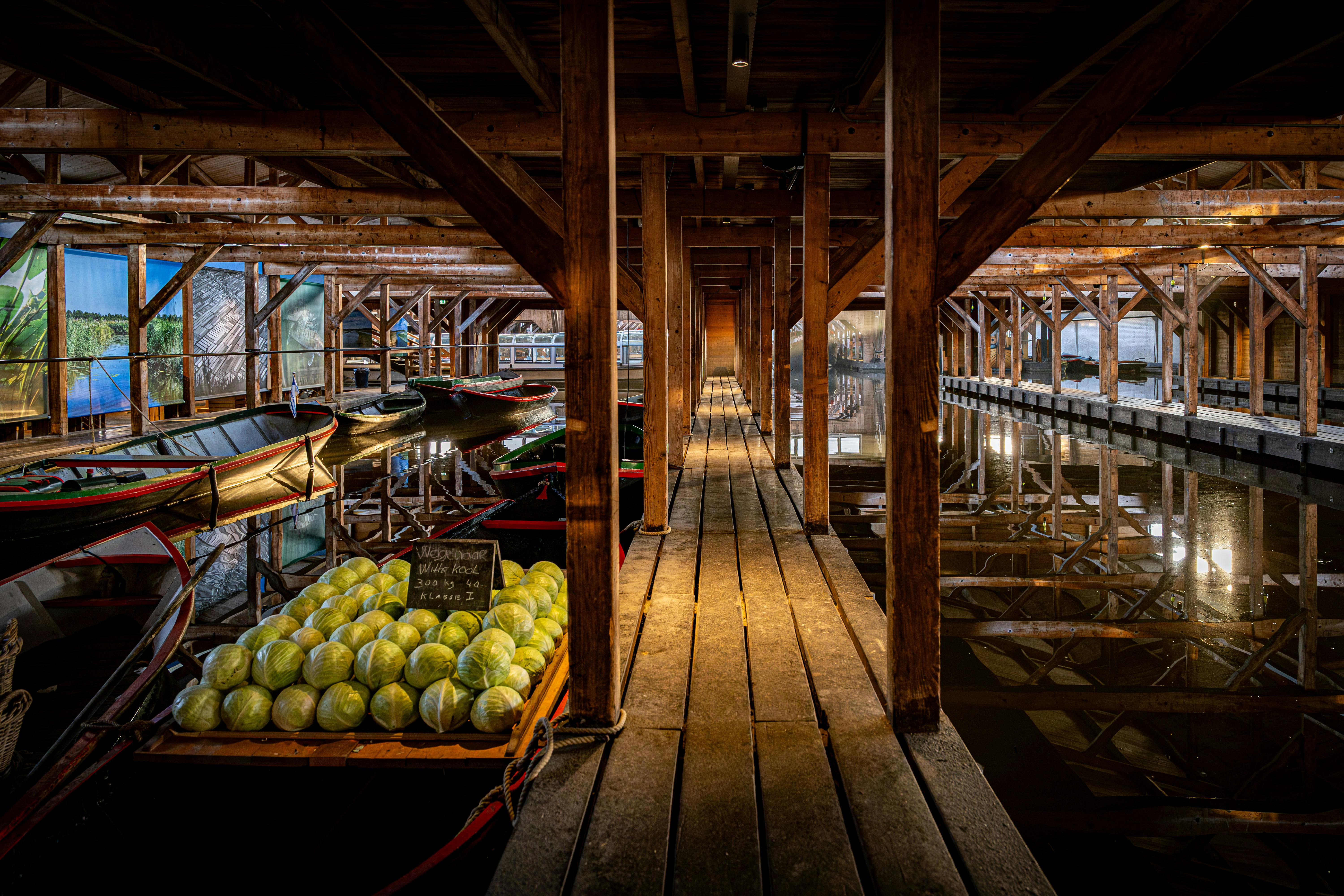 Twee kinderen spelen op witte ladingnetten die boven een waterpartij hangen in een houten gebouw met zichtbare balken en netten.