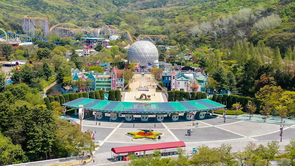An amusement park entrance with colorful buildings, a dome structure, and a roller coaster in the background.